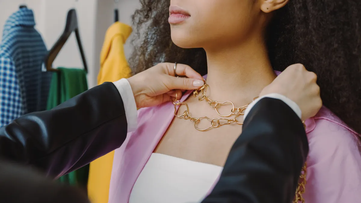 Person fitting a chunky gold chain necklace on a woman