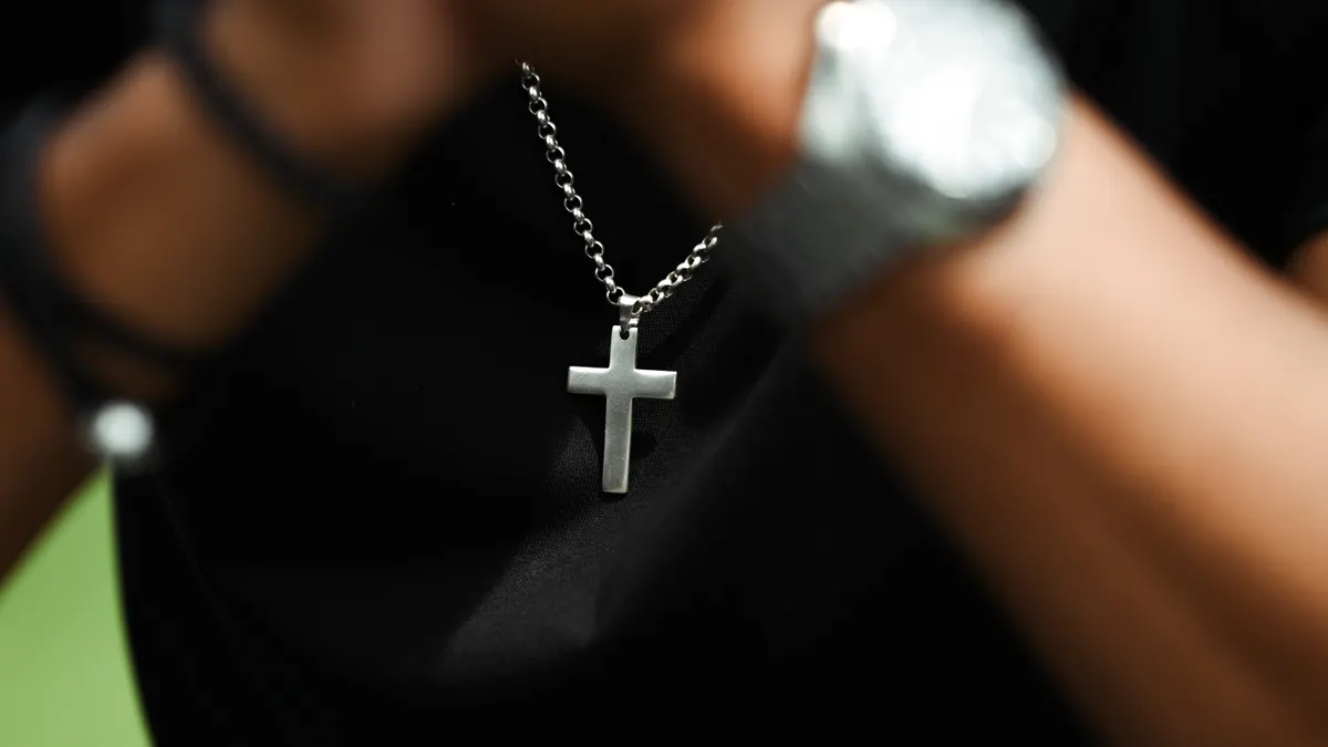 Silver cross pendant necklace worn by a person